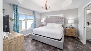 A bedroom with a large bed, a chandelier, a TV, and a view of the outdoors. - Deja Blue with a Stunning View! - 3/2 in Atwood Bungalows w/WATERFRONT BIRDS & SUNSET VIEWS (Atwood Bungalows, The VIllages)