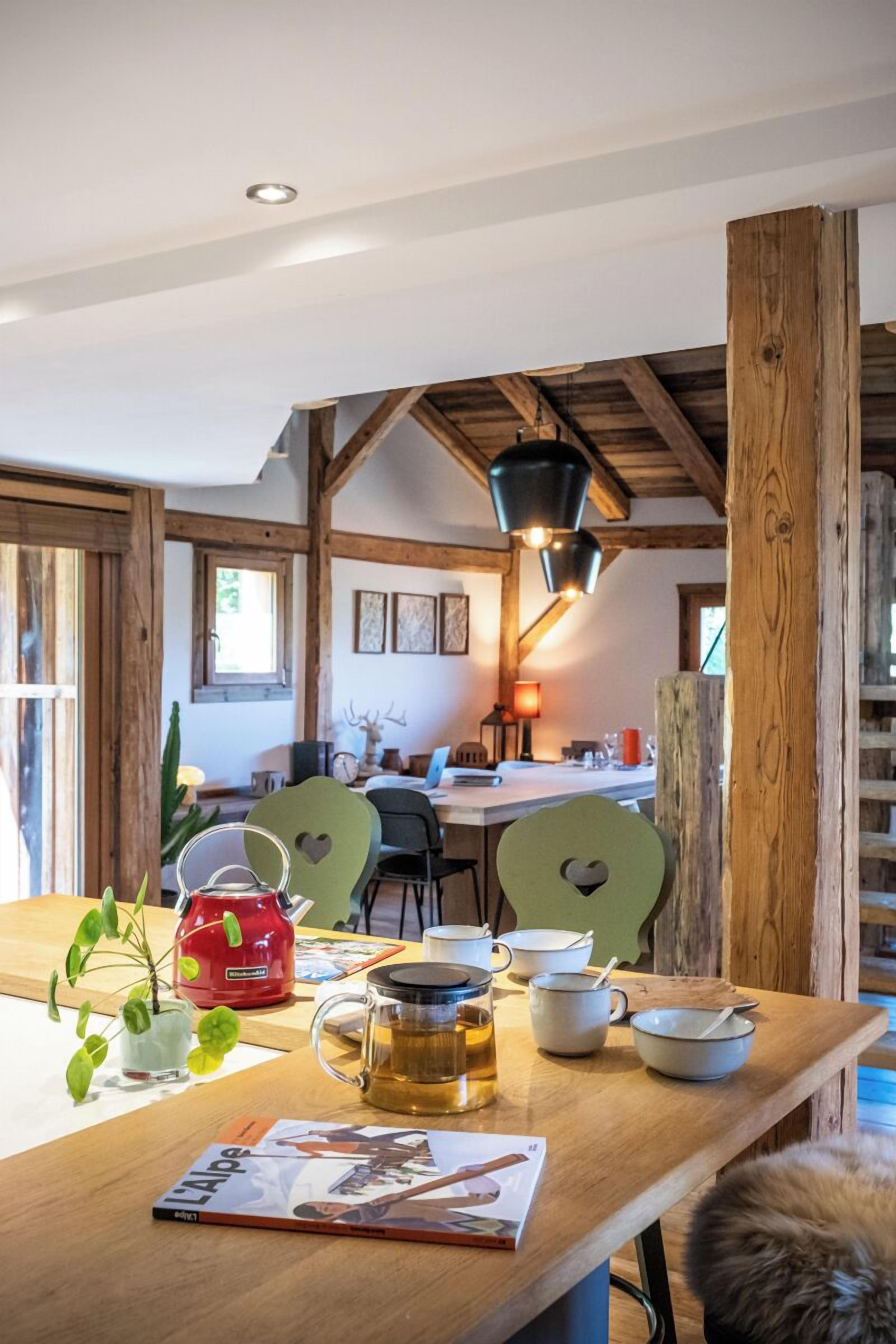 A rustic dining area with wooden beams, a table with a red kettle, a mug, and a magazine.