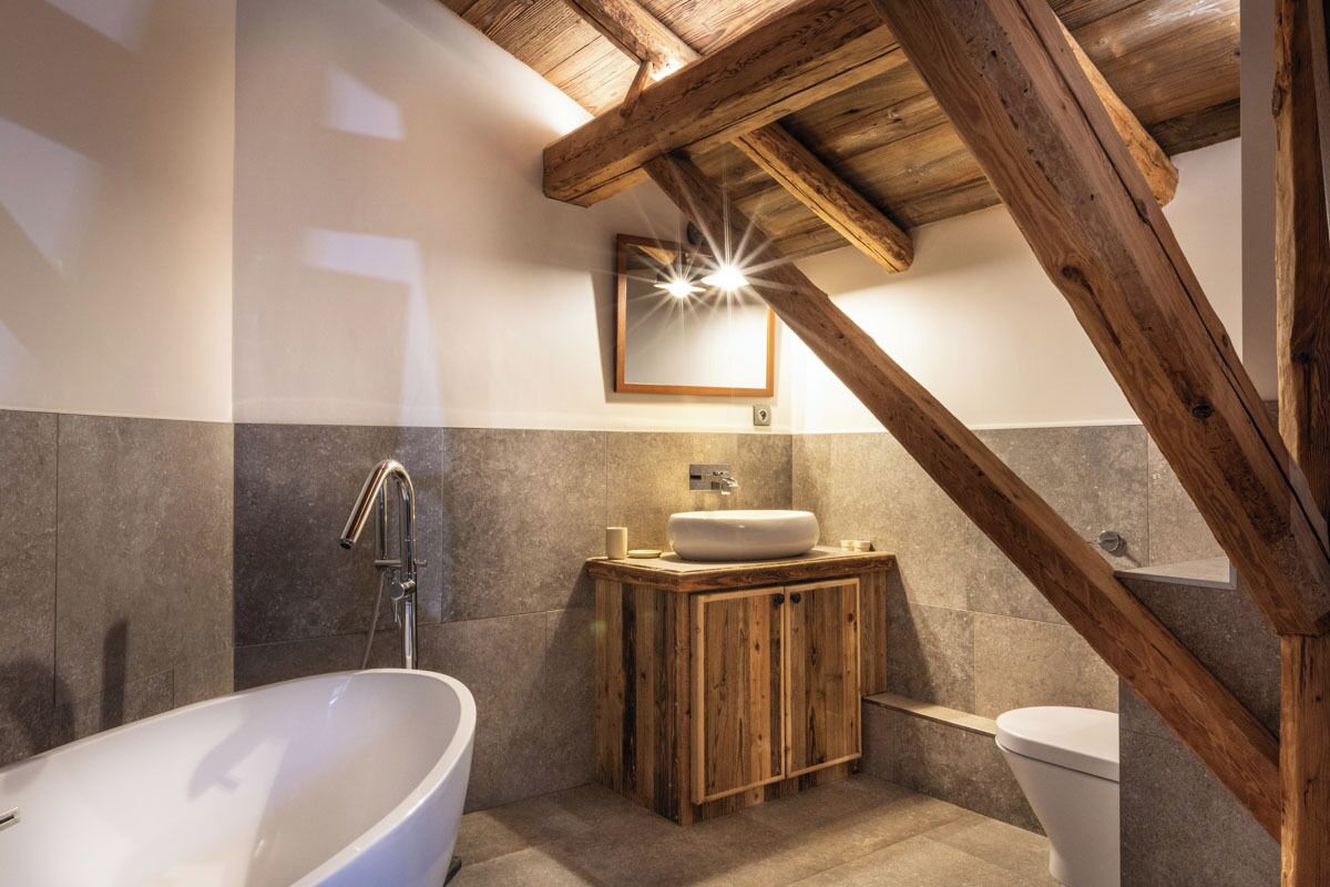 Un baño con bañera independiente, tocador de madera y espejo sobre el lavamanos.