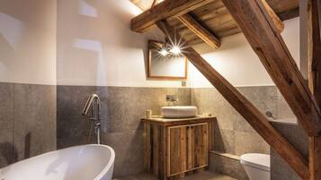 Un baño con bañera independiente, tocador de madera y espejo sobre el lavamanos.