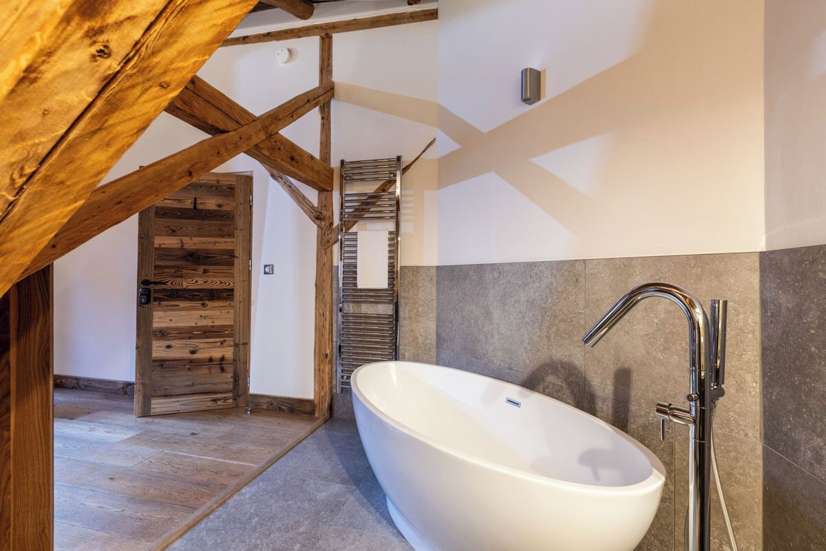 Un baño moderno con una bañera independiente, vigas de madera y suelo de baldosas.