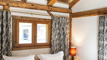 A bedroom with a wooden ceiling, a bed with white bedding, patterned pillows, and curtains with a geometric design.