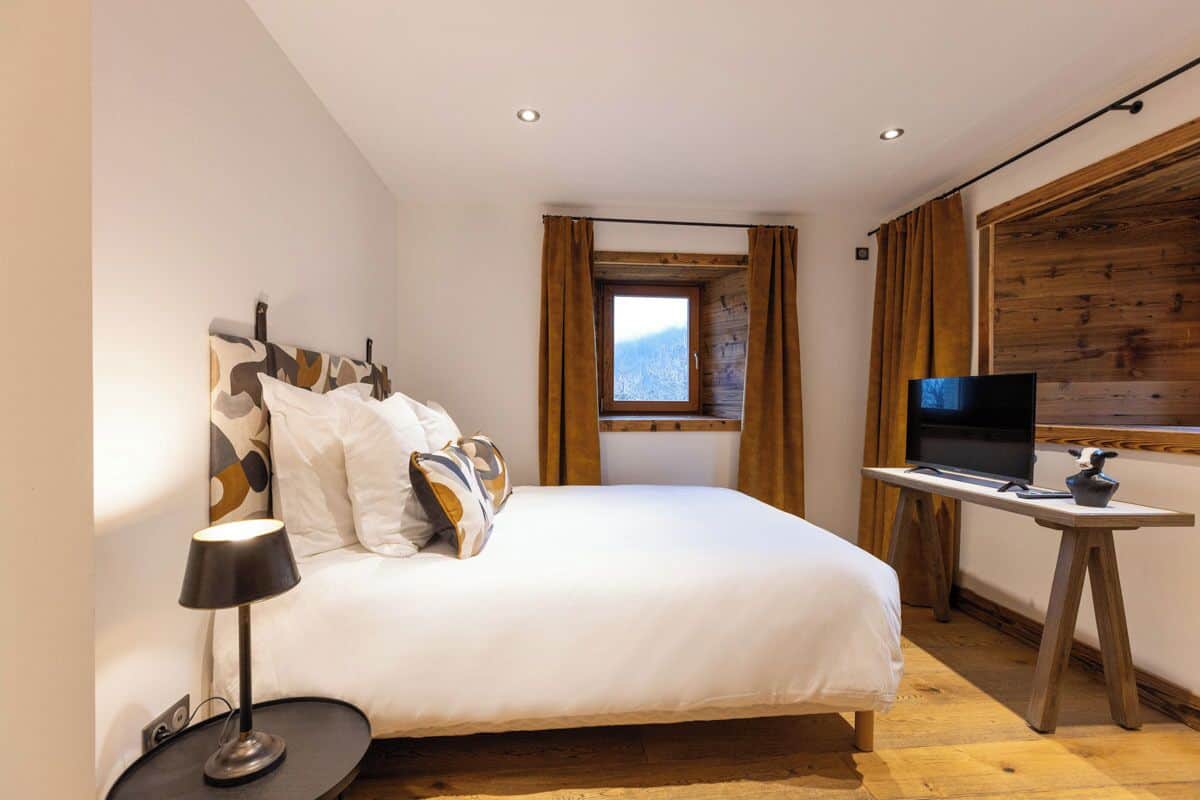 Ein Schlafzimmer mit Bett, Fernseher auf einem Holzboden und einem Fenster mit Vorhängen.