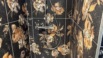 A bathroom with black floral tiles, a shower with a handheld showerhead, and a white sink.