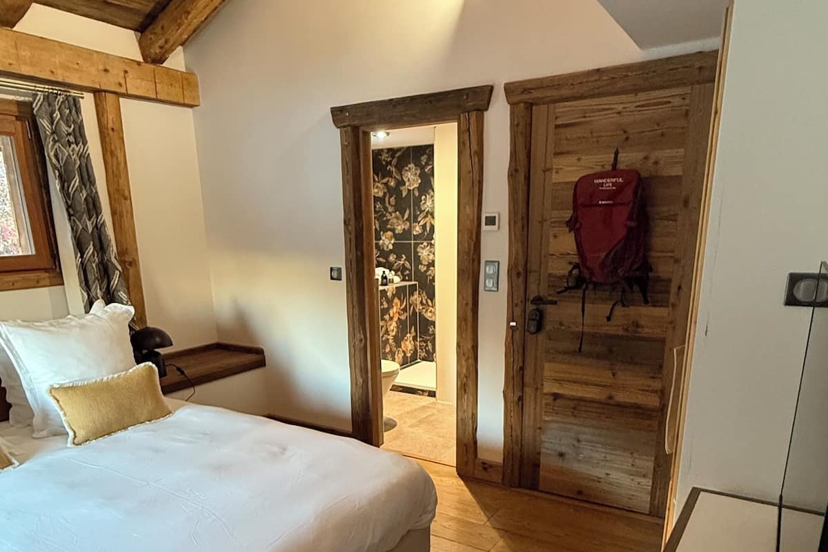 Ein Schlafzimmer mit einem großen Bett, Holzboden, Holzbalkendecke und einer Tür zu einem Badezimmer.