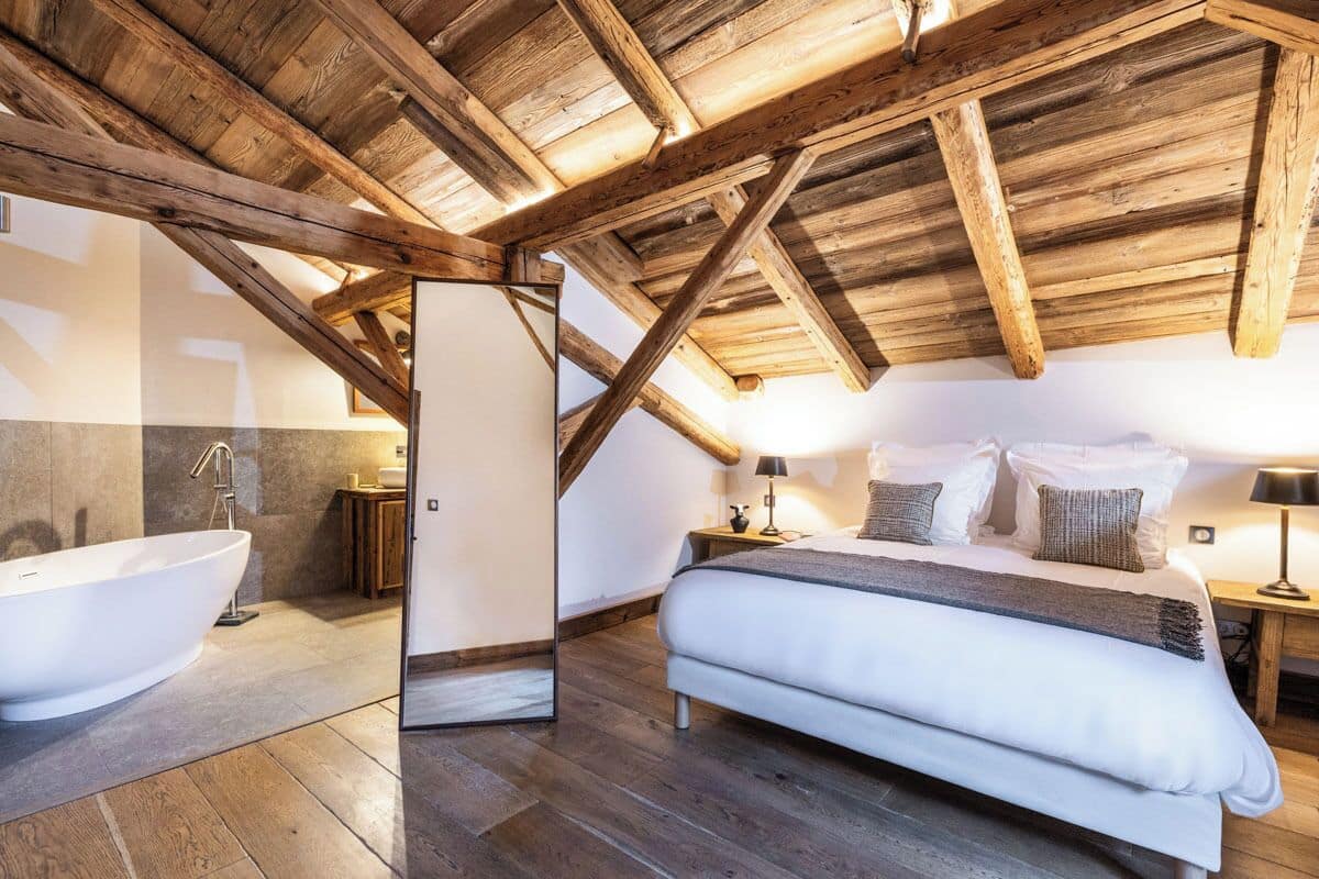 Ein Schlafzimmer mit einem großen Bett, einer Holzbalkendecke, einer Badewanne und einem Nachttisch mit Lampe.