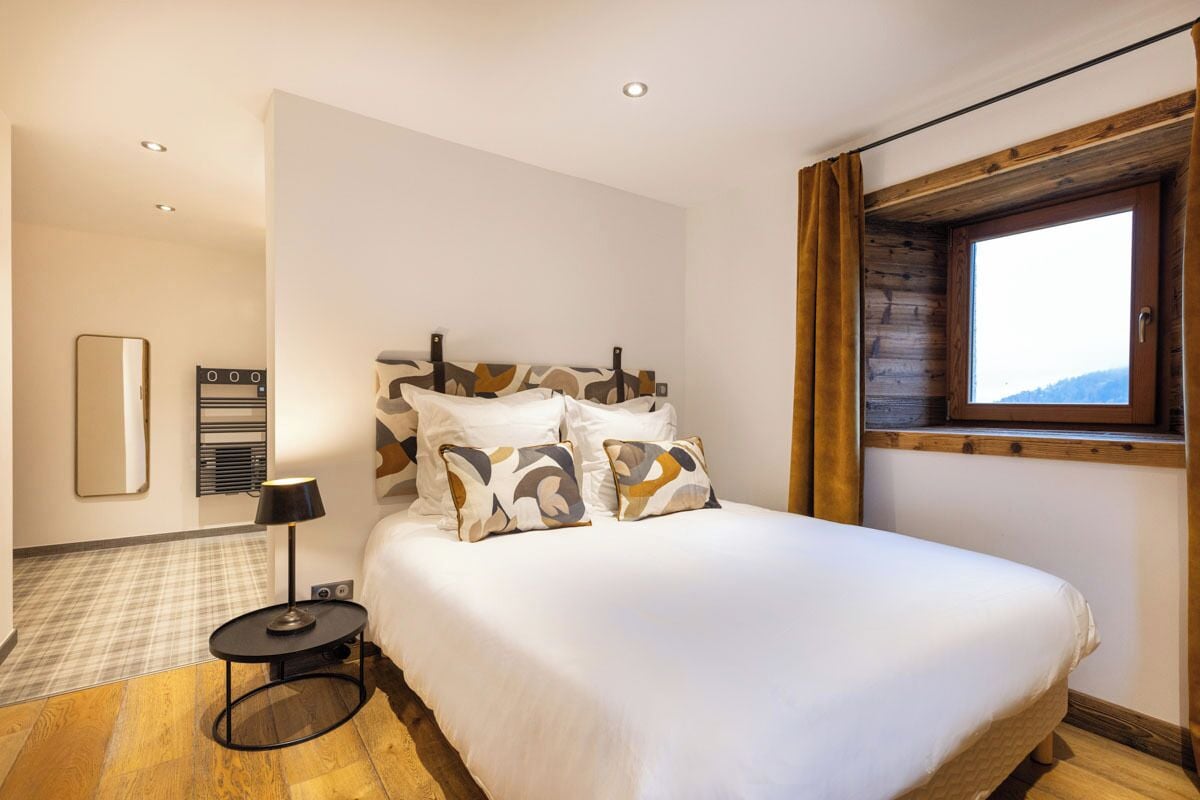 Ein Schlafzimmer mit einem großen Bett, einem runden Nachttisch, einem Spiegel und einem Fenster mit Vorhängen.