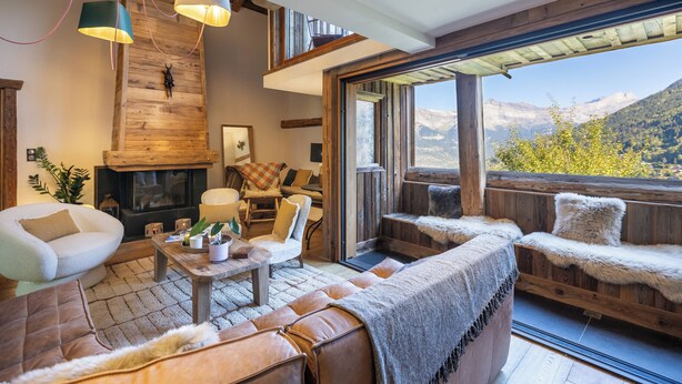 A cozy living room with a fireplace, comfortable seating, and a large window offering a mountain view.