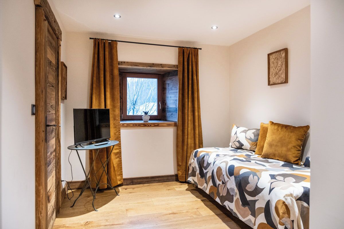Une chambre à coucher avec un lit, une télévision et une fenêtre avec des rideaux.
