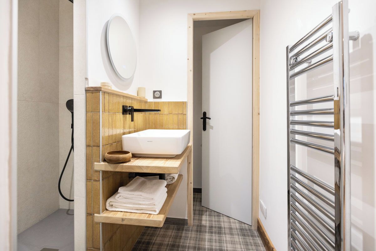 A compact bathroom with a white sink, wooden shelves, a mirror, and a towel rack.
