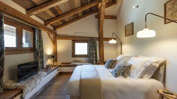 A bedroom with a wooden ceiling, a large bed, a TV, and a window with curtains.