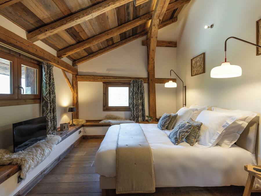 A bedroom with a wooden ceiling, a large bed, a TV, and a window with curtains.