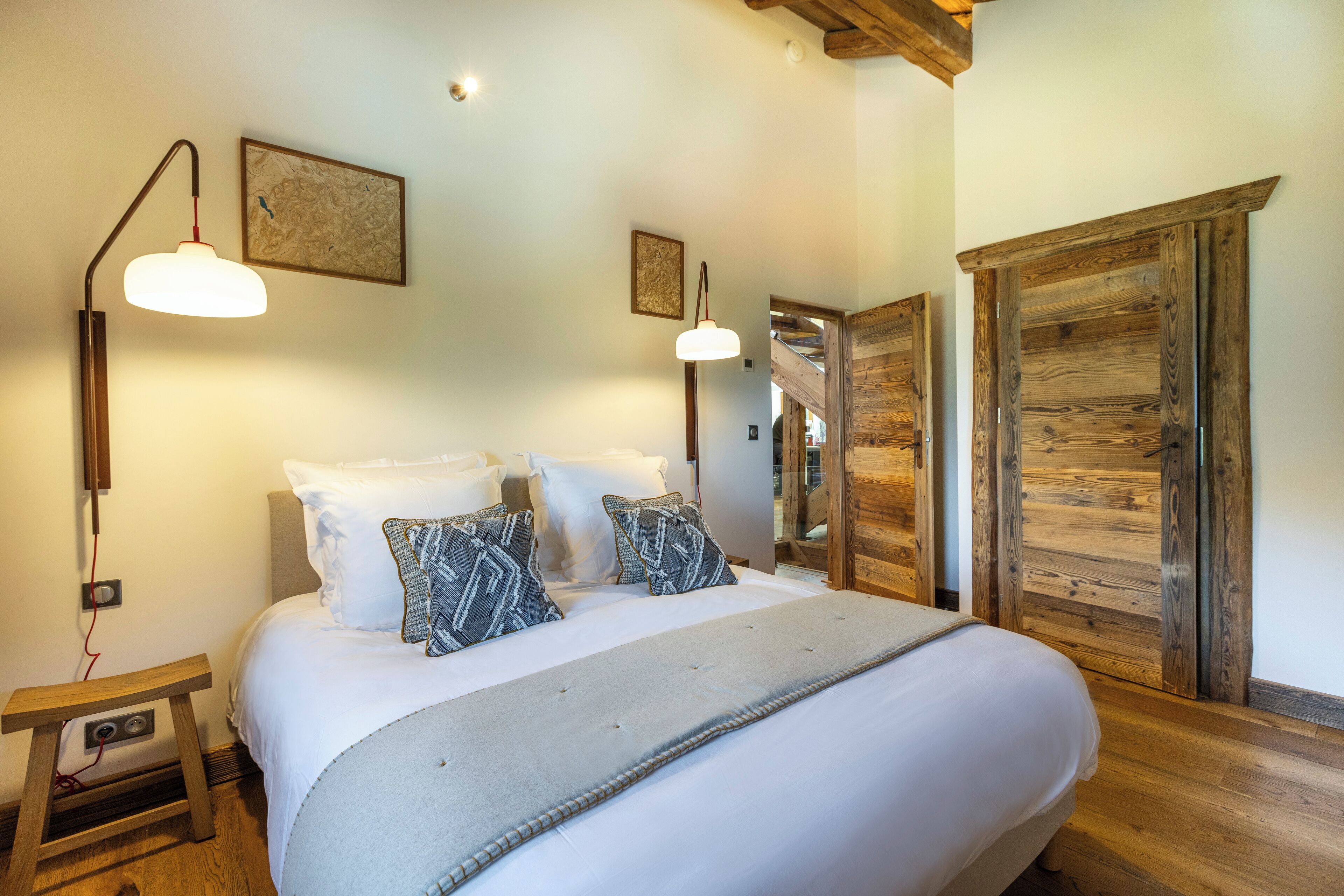 Een slaapkamer met een groot bed, twee bedlampjes, een houten kledingkast en een klein nachtkastje.