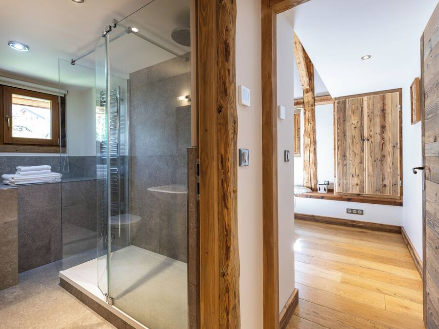 A modern bathroom with a glass shower, wooden accents, and a large mirror.