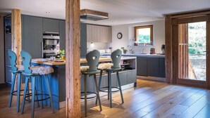 A modern kitchen with bar stools, a large window, and a wooden ceiling.