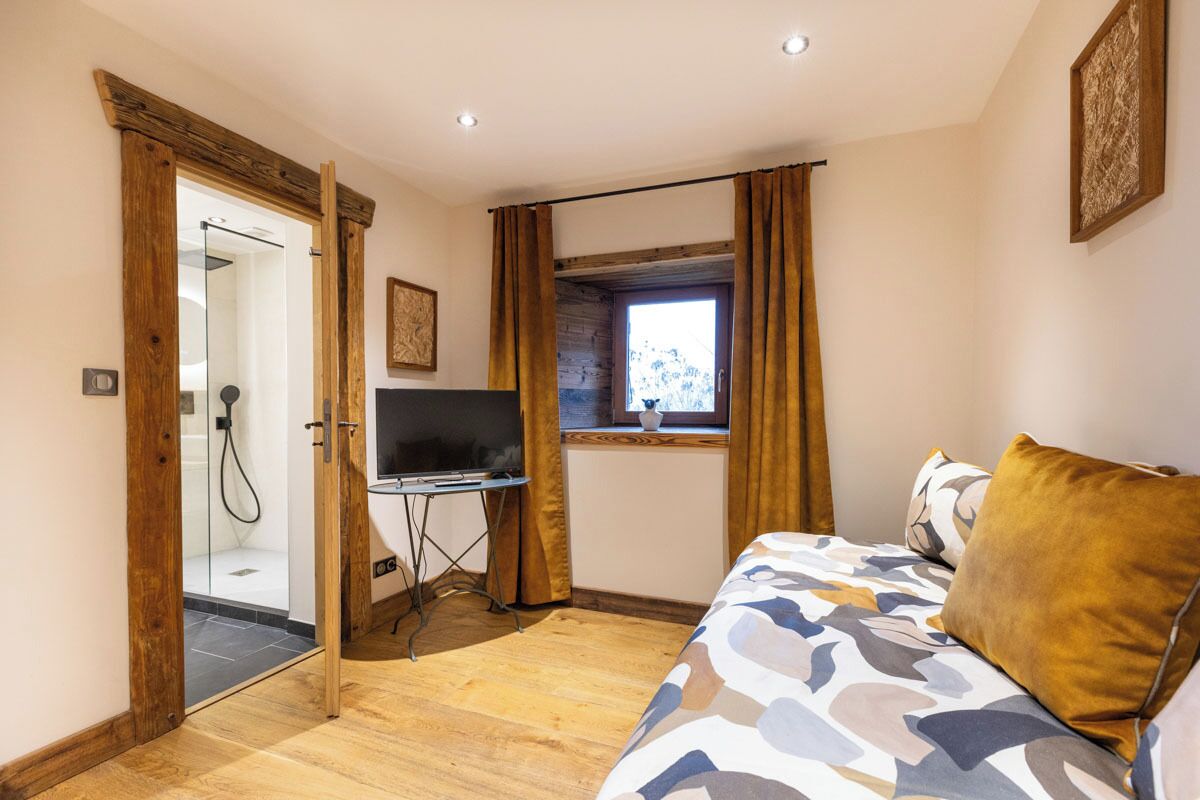 A bedroom with a bed, a TV, a window with curtains, and a shower area.