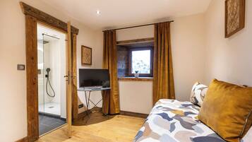 A bedroom with a bed, a TV, a window with curtains, and a shower area.