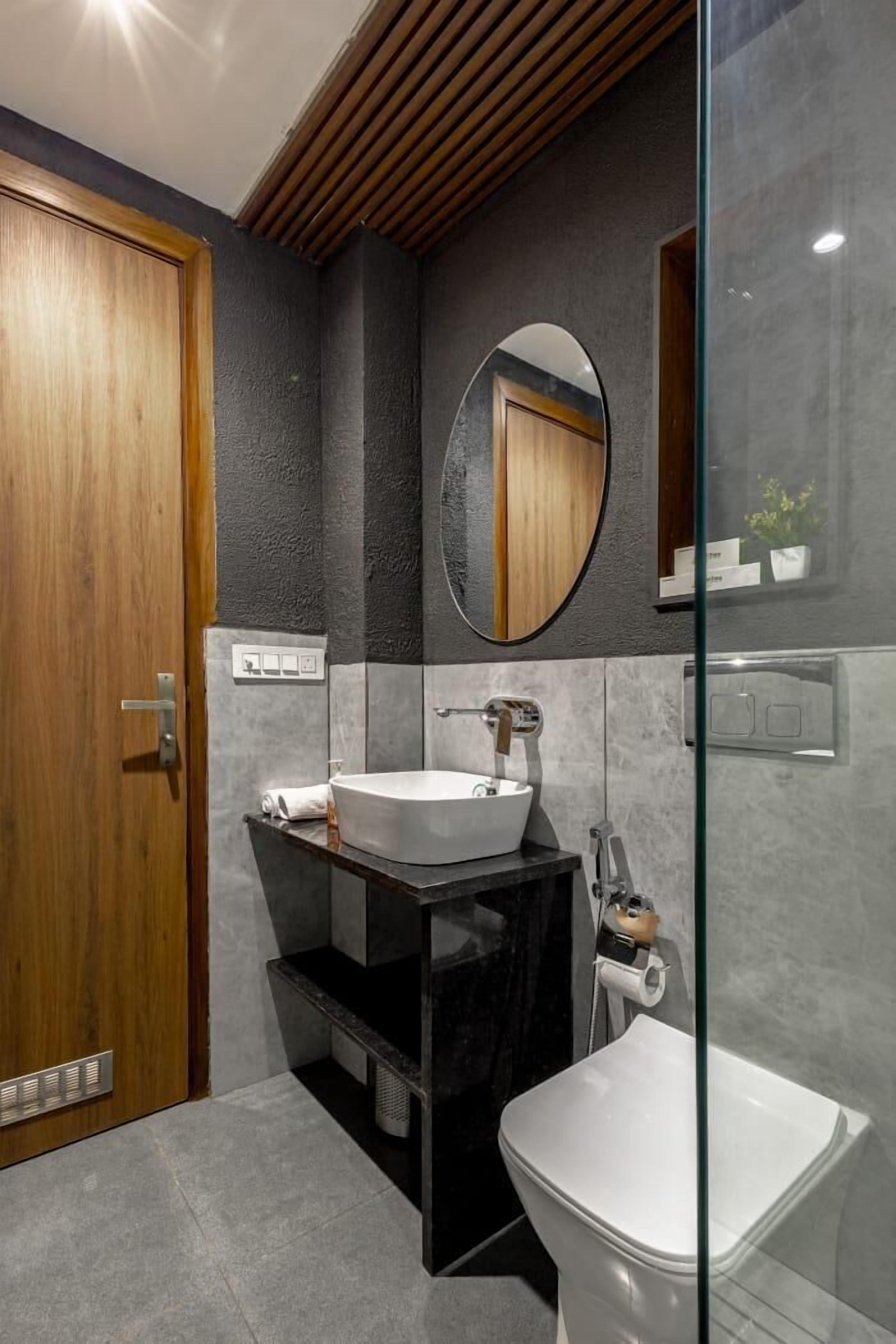 Un baño moderno con puerta de madera, un espejo redondo, un lavabo blanco y un inodoro.