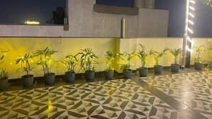 A rooftop terrace with potted plants and a patterned floor, featuring a water tank and a building with a 'UmaTree' sign in the background. - Imperial Stayz (Gurugram)