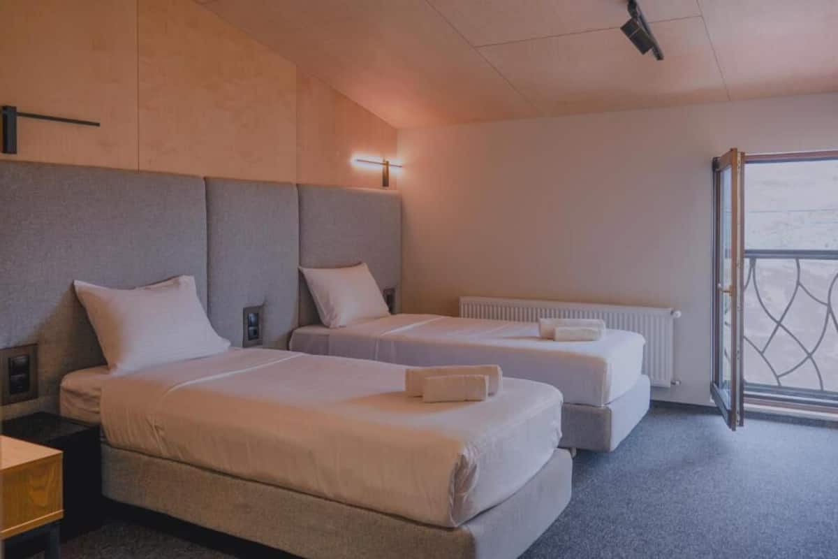 A hotel room with two beds, a radiator, a nightstand, and a window with a view.