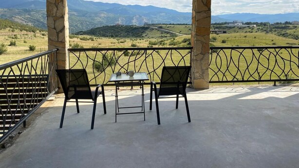 Un espace extérieur abrité, aménagé avec une table et des chaises, des piliers en pierre et offrant une vue sur un paysage montagneux.
