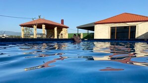Une piscine à l’eau d’un bleu cristallin, un pavillon couvert et un bâtiment avec un toit rouge.