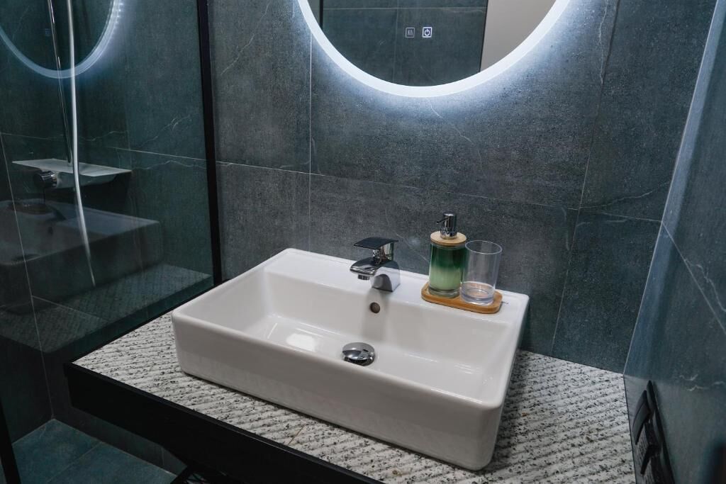 Un baño con lavamanos blanco, un espejo con luz circular y cabina de ducha de vidrio.