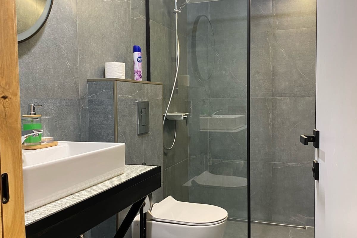 A modern bathroom with a glass-enclosed shower, a white toilet, and a sink with a mirror above it.
