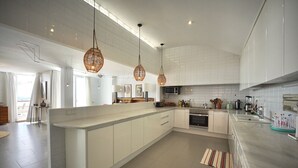 A modern kitchen with white cabinetry, a central island, hanging wicker light fixtures, and a view to the dining area.