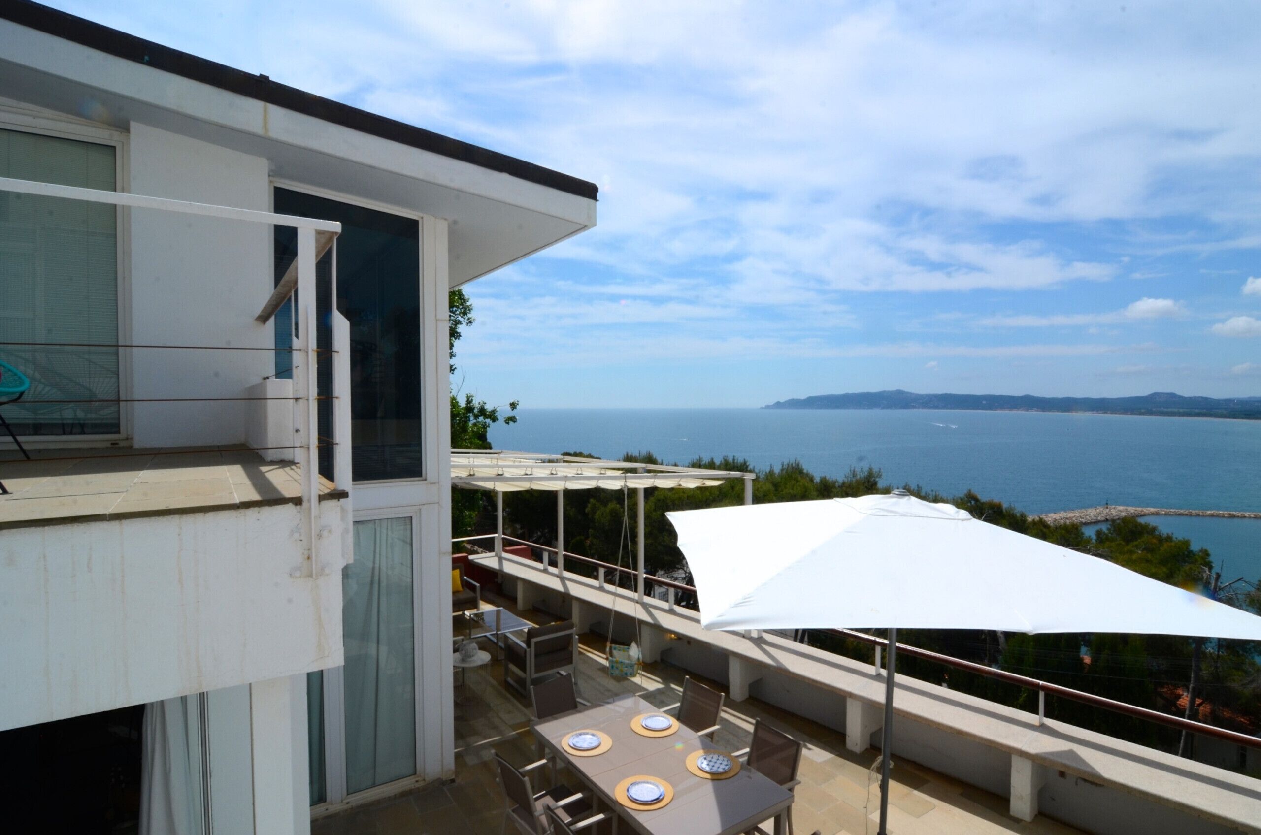 A balcony with a table and chairs, a white umbrella, and a view of the sea.