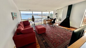 A modern living room with a large window, a red sofa, a desk, and a TV.