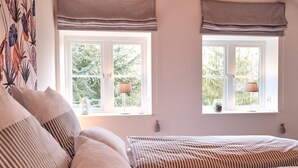 Une chambre à coucher avec un lit, deux fenêtres avec des rideaux et une vue sur la verdure à l’extérieur.