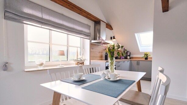 Un coin repas avec une table blanche, des sets de table bleus et des chaises blanches.
