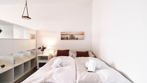 Una habitación de hotel moderna con una cama grande, ropa de cama blanca, una mesita de noche con lámpara, un cuadro en la pared y estanterías empotradas.