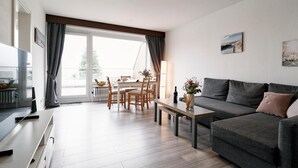 Una sala de estar moderna con un sofá gris, una mesa de comedor con sillas y un televisor sobre un mueble.