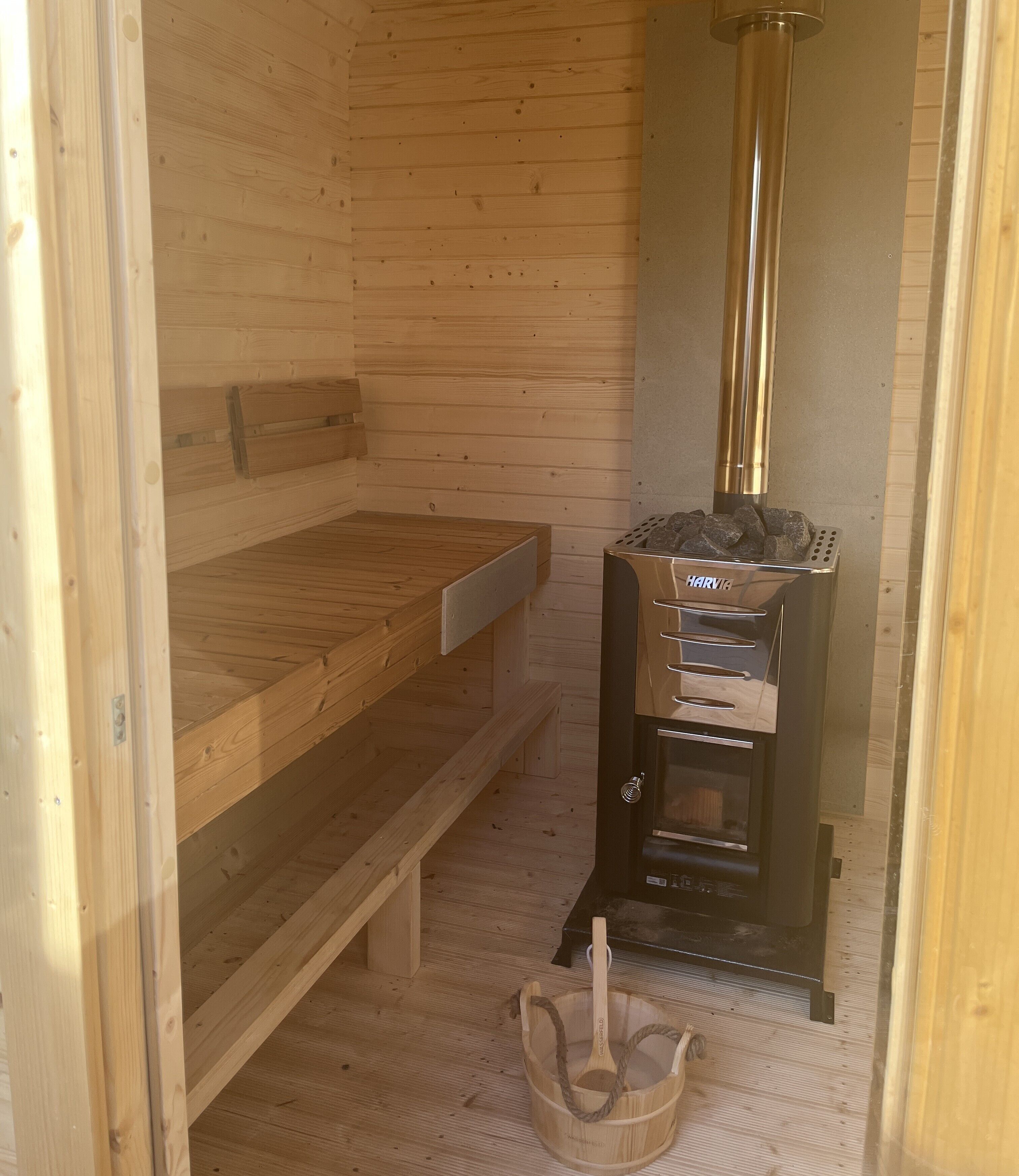 A sauna room with a wooden bench, a stone heater, and a wooden bucket.