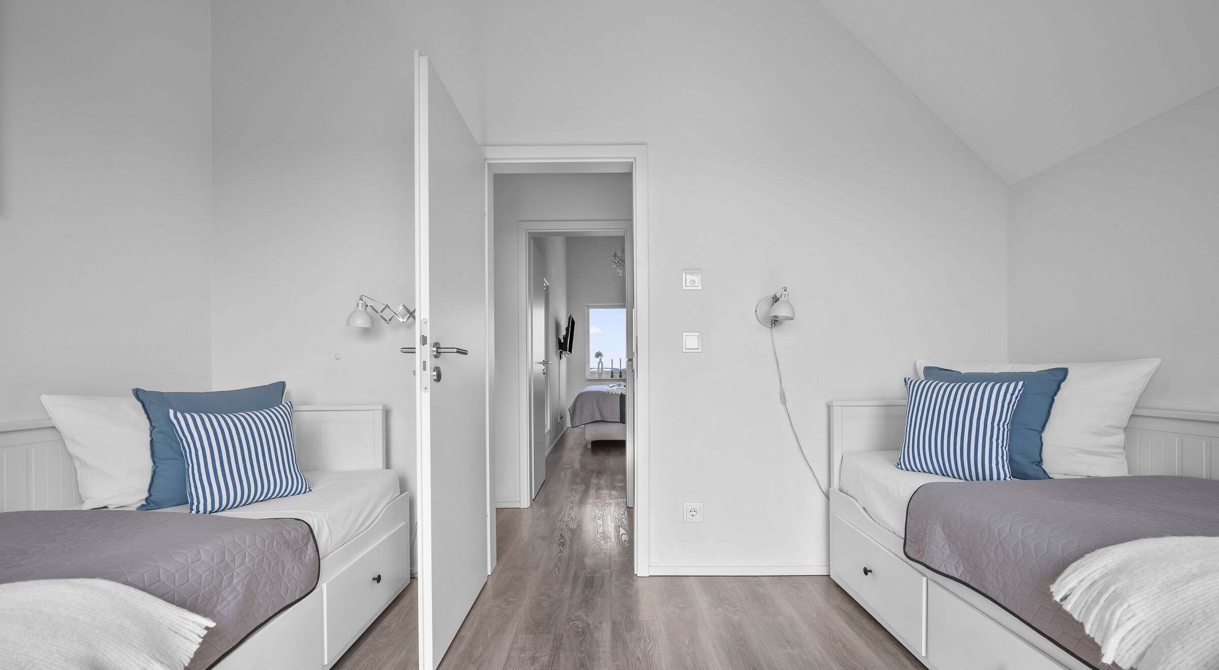 Une chambre moderne avec deux lits, un couloir menant à une salle de bain et une vue sur le ciel.