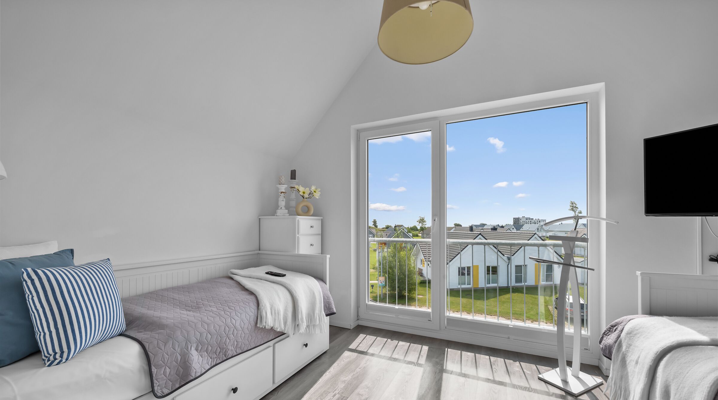 A bedroom with a large window, a bed, a dresser, and a TV.
