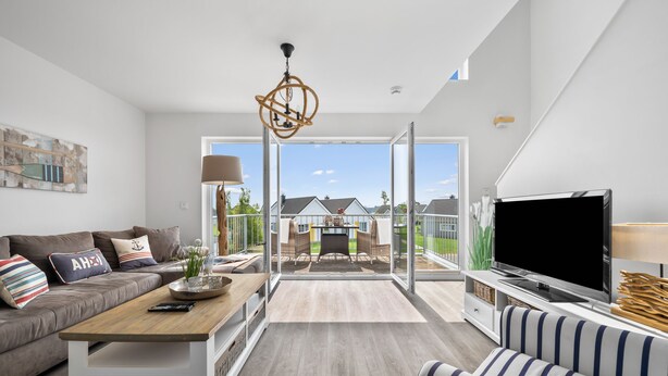 Een moderne woonkamer met een bank, een salontafel, een televisie en een balkon met uitzicht op huizen.