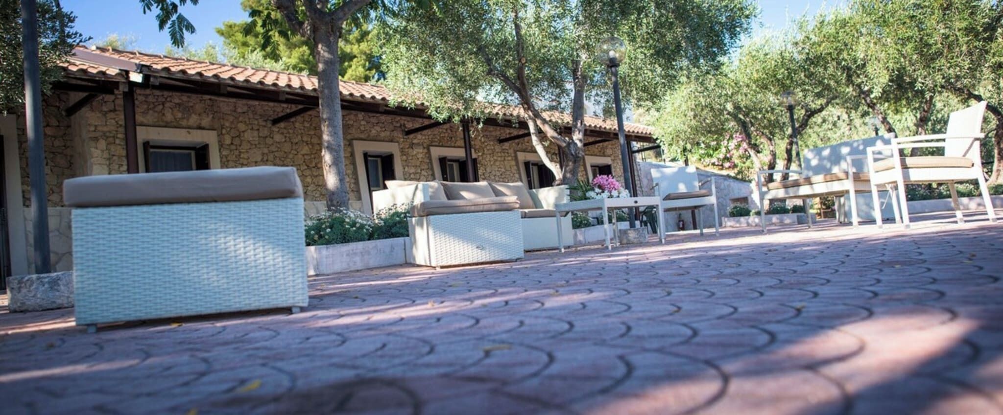 A stone building with a tiled roof, outdoor seating with white cushions, and a paved walkway.