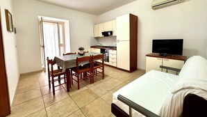 Una habitación compacta con cama, una kitchenette pequeña, una mesa de comedor con sillas y una televisión.