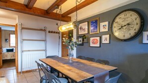 Een eetgedeelte met een houten tafel, grijze stoelen, een grote wandklok en ingelijste foto's.