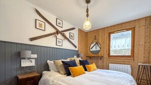 Een slaapkamer met een bed, een houten hoofdbord, een hanglamp, een raam en een radiator.