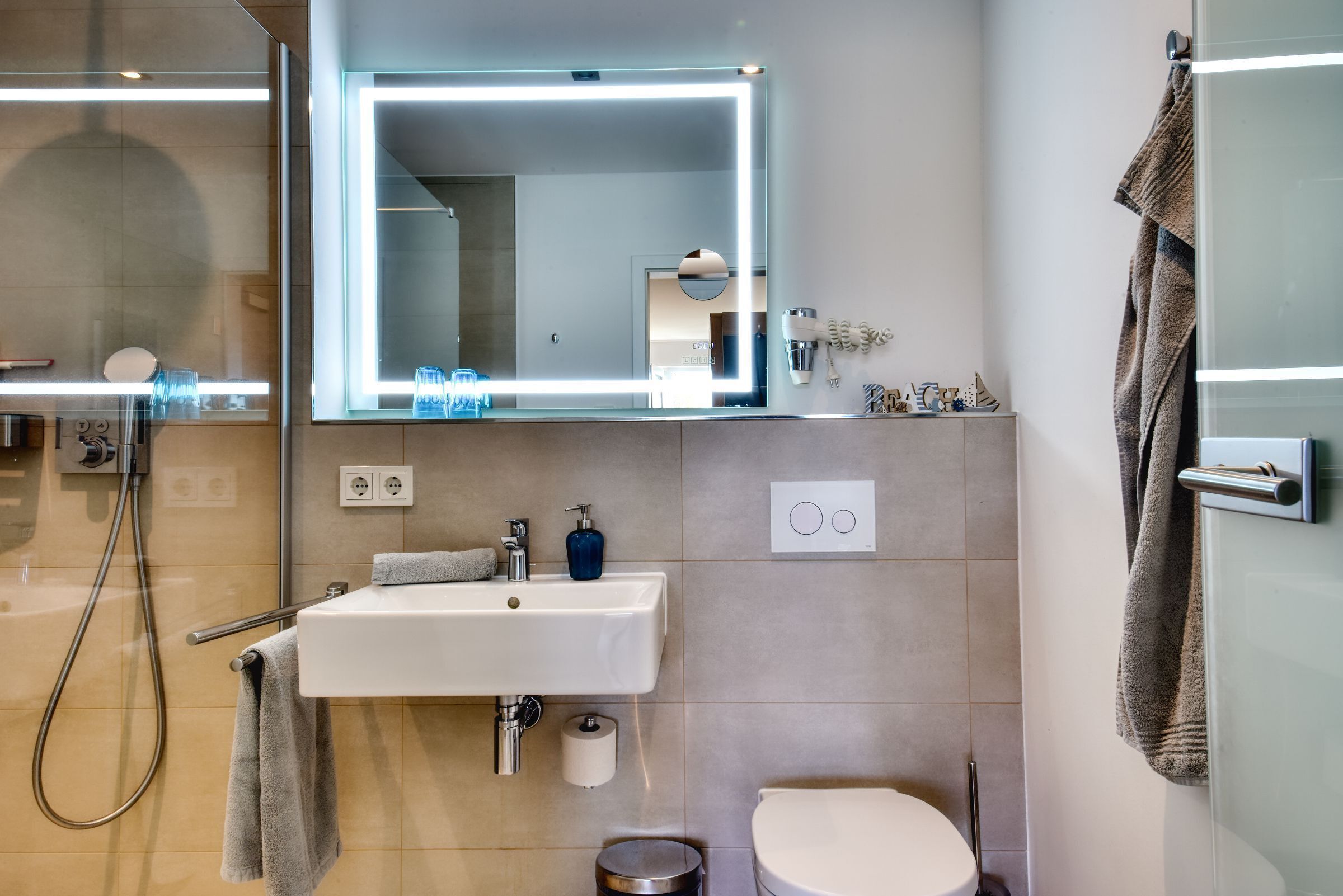 Een moderne badkamer met een grote spiegel, een wastafel, toilet en douche.