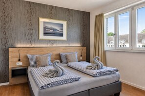 Habitación de hotel con una cama grande, cabecera con un cuadro, ventana con cortinas y vista a edificios.