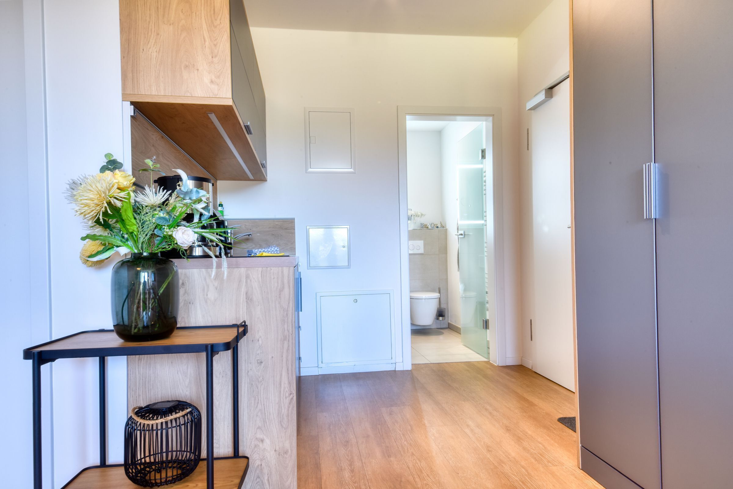 Une cuisine moderne avec des meubles en bois, un plan de travail blanc et un vase de fleurs posé sur une table noire.