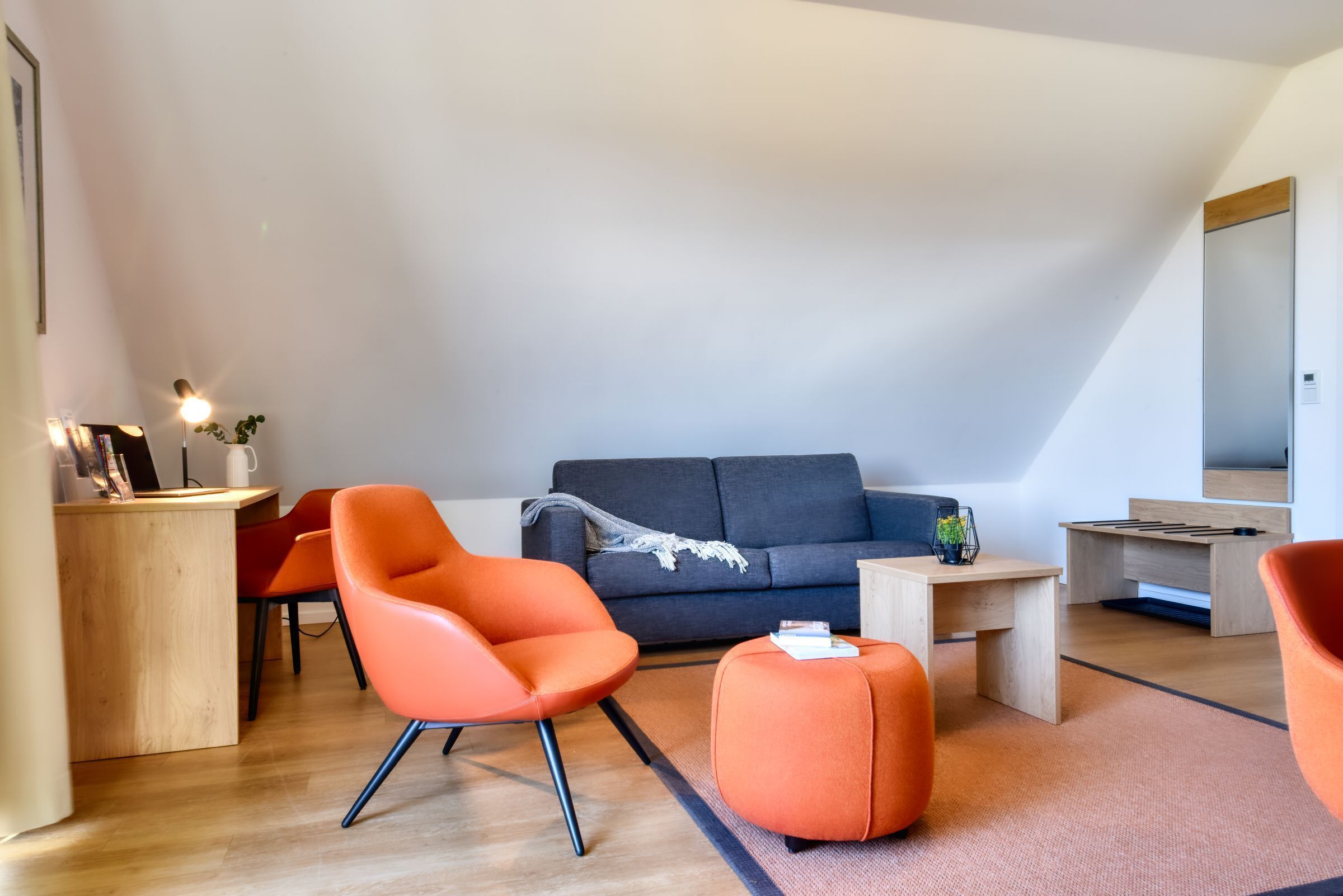 Un salon moderne avec un canapé, des fauteuils orange, un bureau en bois et une petite table.