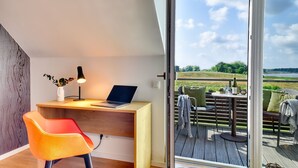 Ein modernes Zimmer mit einem Holztisch, einem Laptop und einem Stuhl. Es verfügt über eine große Schiebeglastür, die auf eine Terrasse mit Tisch und Stühlen führt.