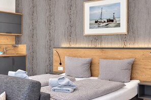 Een moderne hotelkamer met een houten hoofdeinde, een bed met geruit beddengoed, een nachtkastje, een wandtelevisie en een ingelijst schilderij van een boot aan de muur.
