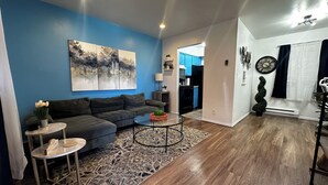 Ein modernes Wohnzimmer mit blauer Akzentwand, einem Ecksofa, einem Couchtisch und einem Teppich.